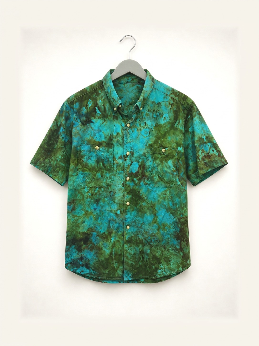 Hand ice-dyed cotton shirt in green and teal on a wooden hanger