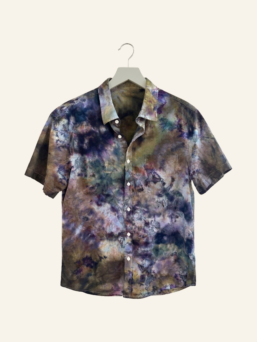 Hand ice-dyed cotton short-sleeve shirt in layered violet, indigo, olive, and cream on a pale grey hanger
