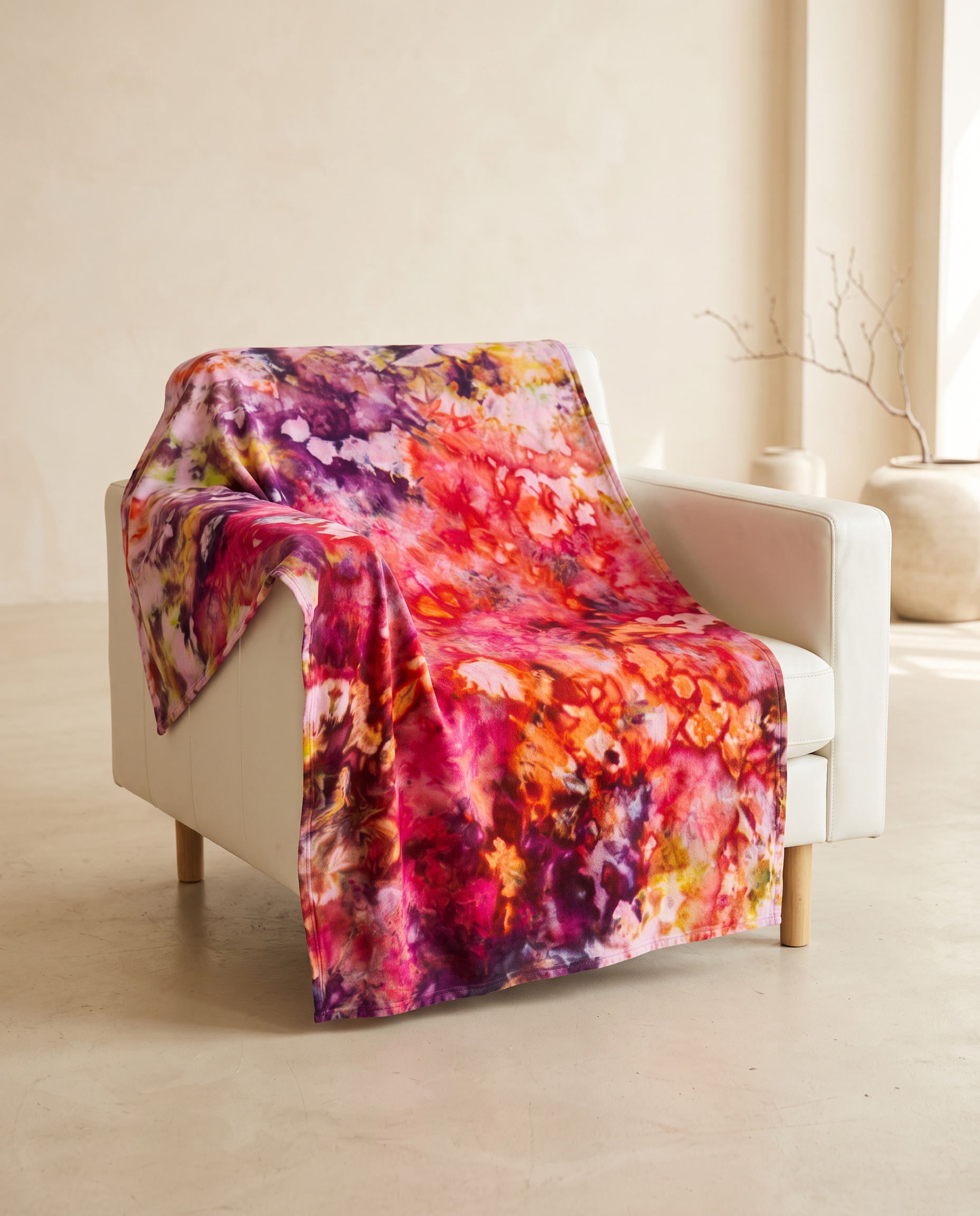 Hand ice-dyed blanket in magenta, chartreuse, peach, apricot and lilac draped over a white leather armchair