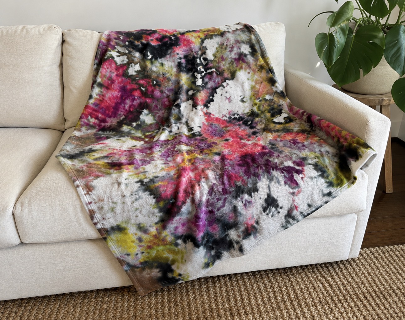 Hand ice-dyed cotton blanket in magenta, charcoal and citron draped over a cream sofa